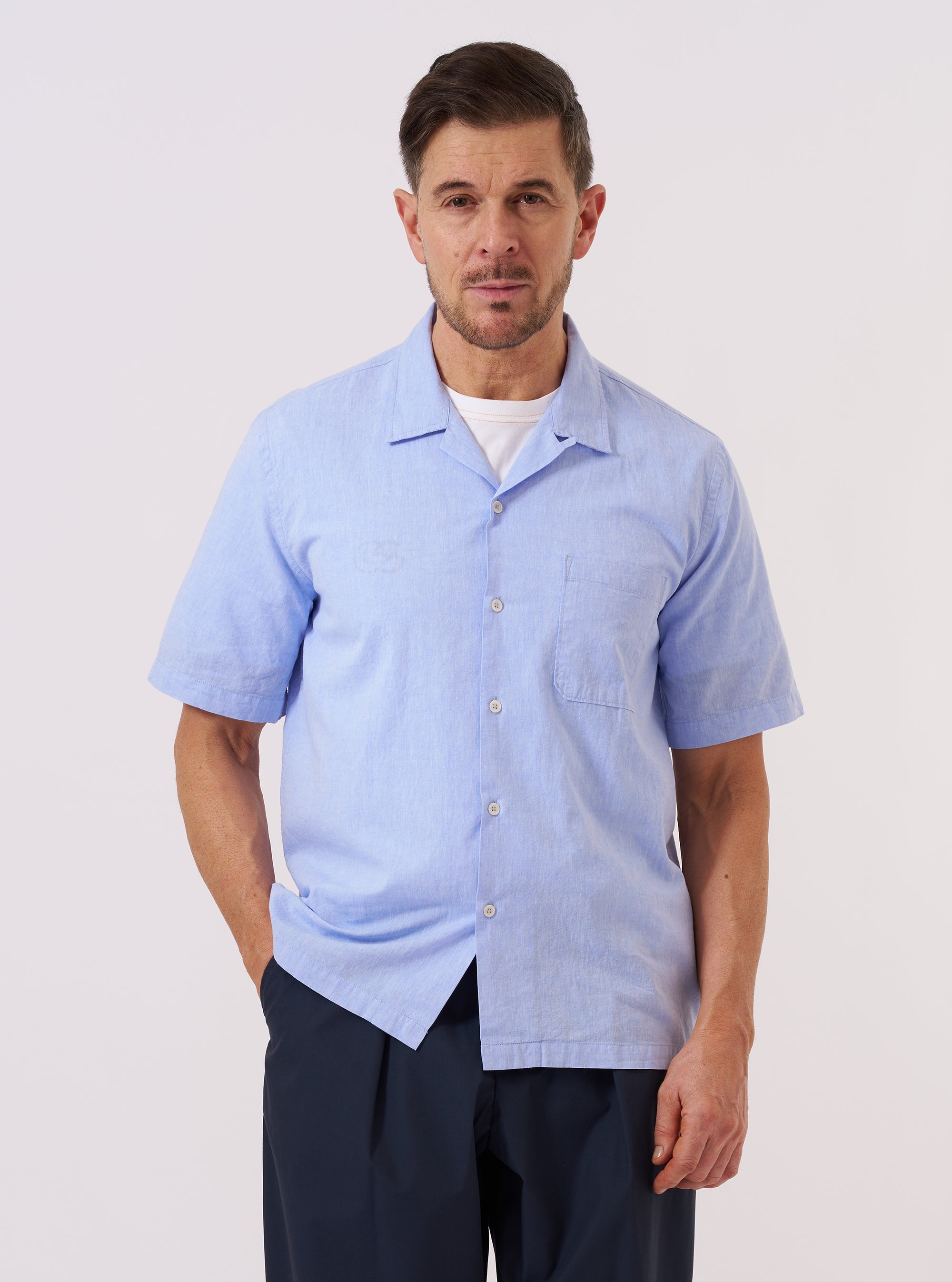 A model wears the Sky Blue Sido Linen Mix Road Shirt while standing against a plain, neutral background. The shirt features a relaxed camp collar with a loop-close button at the neck, a central button-down front, and a single patch pocket on the left chest. The sky blue fabric has a subtle, textured appearance characteristic of a cotton-linen blend.