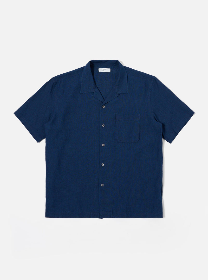 The Indigo Lincot Denim Road Shirt is presented as a flat lay against a plain white background. The short-sleeved shirt features a camp collar, a six-button front closure with contrasting white buttons, and a single patch pocket on the left chest. The indigo-dyed fabric shows a fine denim texture from the cotton and linen blend.