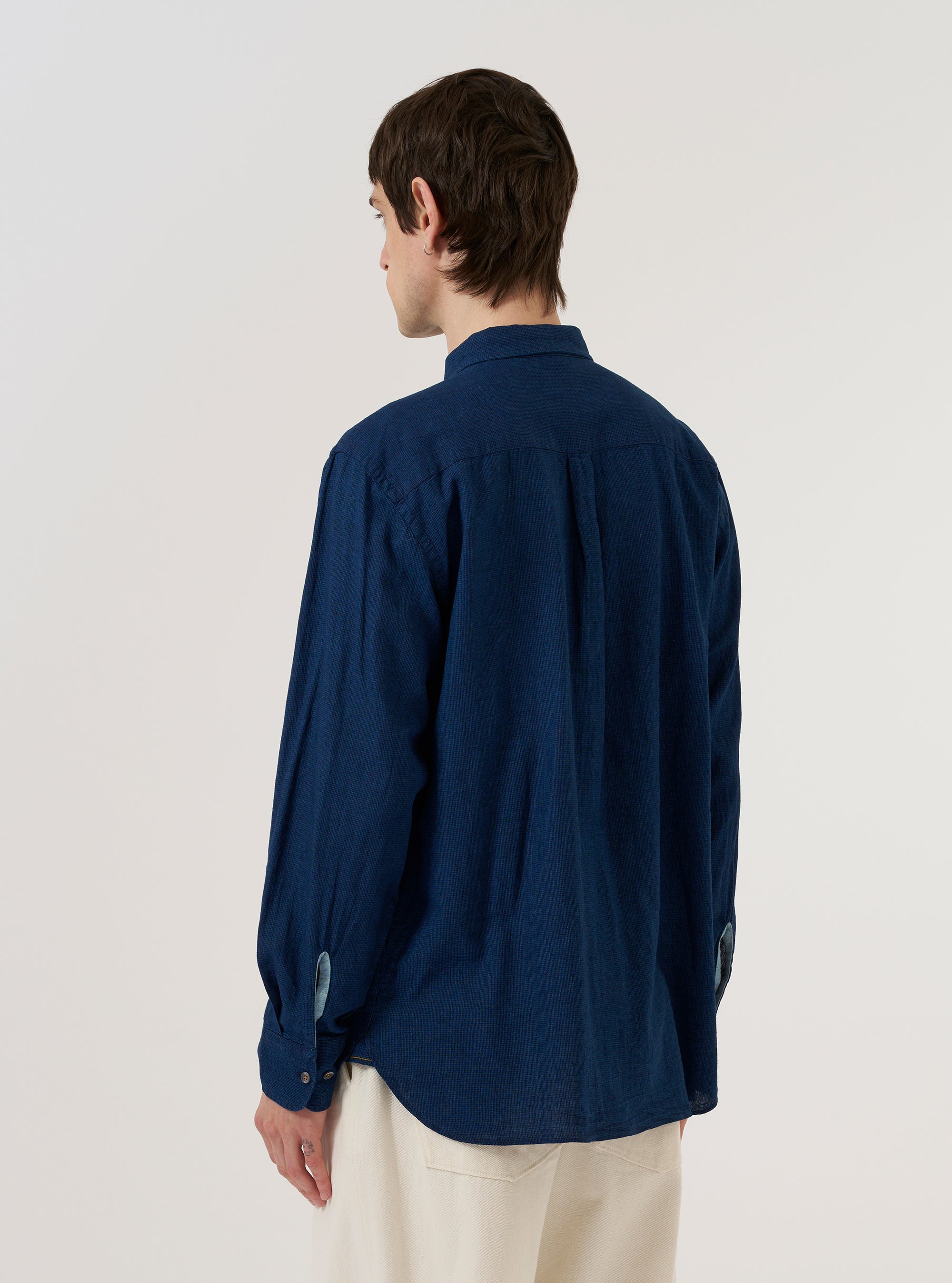 A model wears the Indigo Lincot Denim Lazy Day Shirt, shown from a rear three-quarter angle against a plain white background. The shirt features a relaxed fit, a straight hem, and a simple collar. The dark indigo blue fabric has a textured appearance, characteristic of the cotton and linen denim blend.