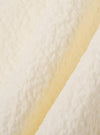 A close-up fabric swatch of the Ecru Arten Seersucker Road Shirt highlights the off-white ecru color and the distinct puckered texture of the organic cotton seersucker fabric. The material fills the frame, providing a detailed view of the textile's construction.