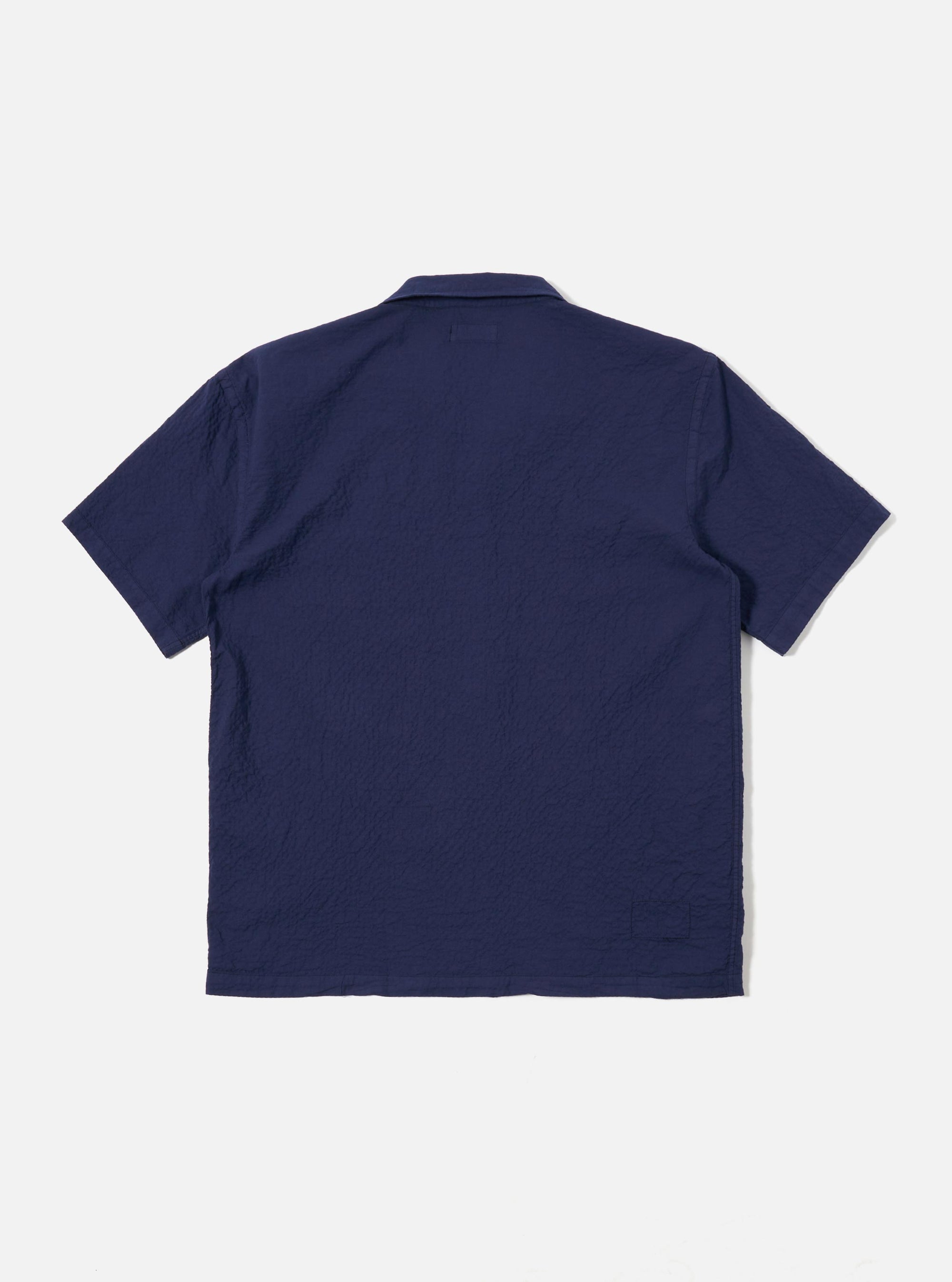 The Navy Arten Seersucker Road Shirt is shown from the back as a flat lay against a plain white background. The image highlights the garment's straight hem and the distinct puckered texture of the navy blue seersucker fabric.