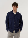 A model wears the Navy Arten Seersucker Attendant Shirt against a plain white background. The shirt features a loose fit, a one-piece collar, a central button closure, and two large oversized flap pockets on the chest. The deep navy fabric has a distinct puckered seersucker texture.