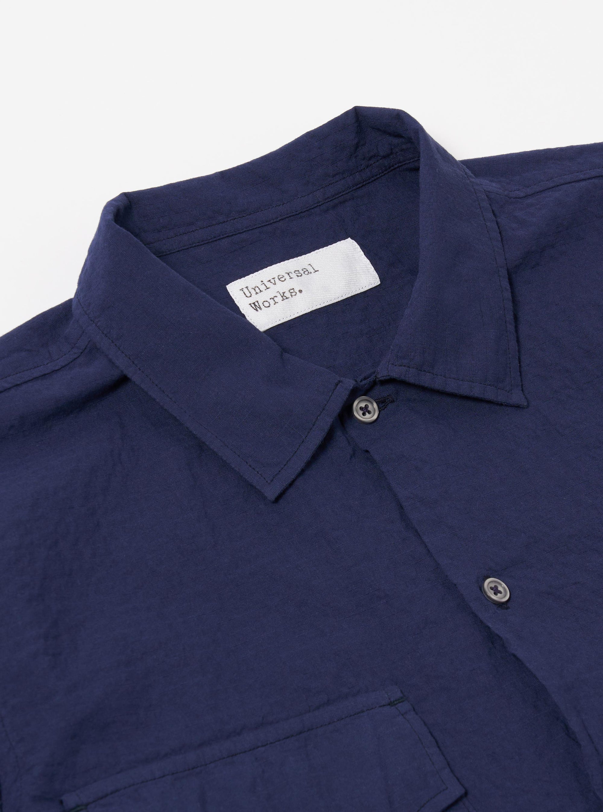 The Navy Arten Seersucker Attendant Shirt is shown from the back as a flat lay against a plain white background. The image highlights the shirt's straight hem, short sleeves, and the distinct puckered texture of the navy blue seersucker fabric. A simple yoke and a central vertical seam are visible on the rear panel.