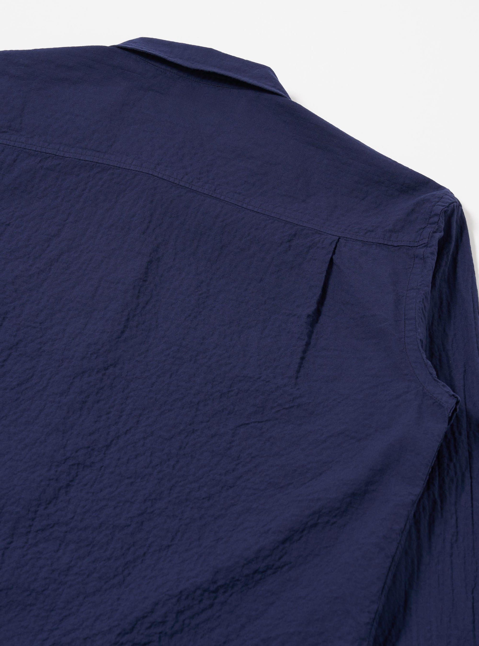 The Navy Arten Seersucker Attendant Shirt is worn by a model against a plain white background. The shirt features a five-button front closure, a simple pointed collar, and three patch pockets, including one at the chest and two at the waist. The dark navy organic cotton fabric has a distinct puckered seersucker texture. The model is shown from a front angle, wearing the shirt buttoned over a light-colored base layer. No mannequin is present in the image.