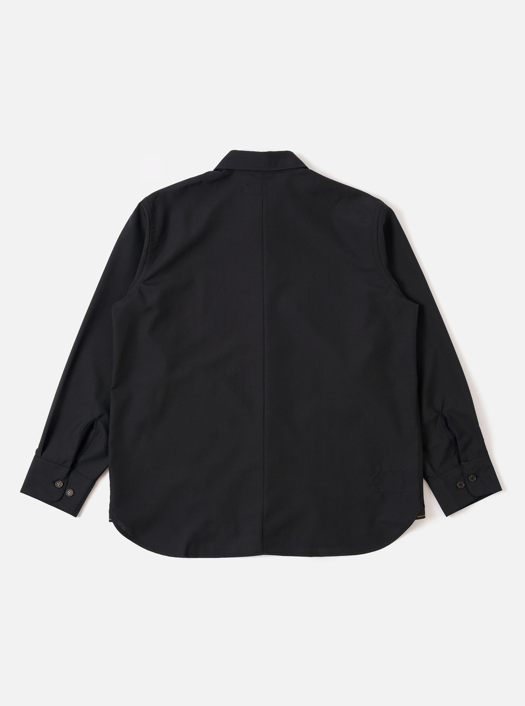 The Black Tropical Suiting Travail Overshirt is shown from the back as a flat lay against a plain white background. The image highlights the clean, simple construction of the garment's rear and the smooth texture of the black wool-blend tropical suiting fabric.
