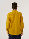A model wears the Golden Brown Organic Fine Poplin CPO Shirt, shown from the back against a plain white background. The shirt features a structured collar, a straight hem, and long sleeves with buttoned cuffs. The smooth texture of the golden brown organic poplin fabric and the clean horizontal back yoke are prominent features.