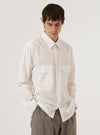 A model wears the Ecru Organic Fine Poplin CPO Shirt over a dark-colored top, standing against a plain, neutral studio background. The shirt features a pointed collar, a central button-down closure, and two large buttoned patch pockets on the chest. The ecru-colored organic cotton poplin fabric has a smooth, fine texture and a clean, utility-inspired appearance.