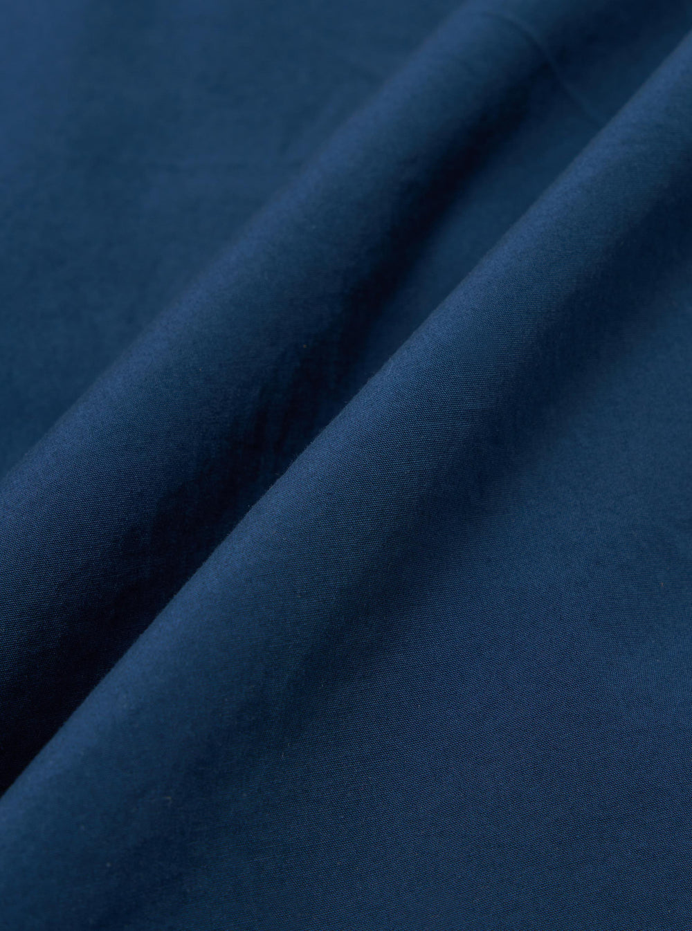 A close-up fabric swatch of the Navy Organic Fine Poplin CPO Shirt shows a deep navy blue color with a smooth, tightly woven poplin texture. The material is displayed in a way that highlights its fine grain and matte finish.