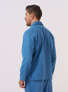 A model wears the Washed Indigo Recycled Herringbone Smock Overshirt, shown from the back against a plain, neutral background. The overshirt features a relaxed pullover fit, a simple collar, and a straight hem. The washed indigo fabric has a visible herringbone texture.