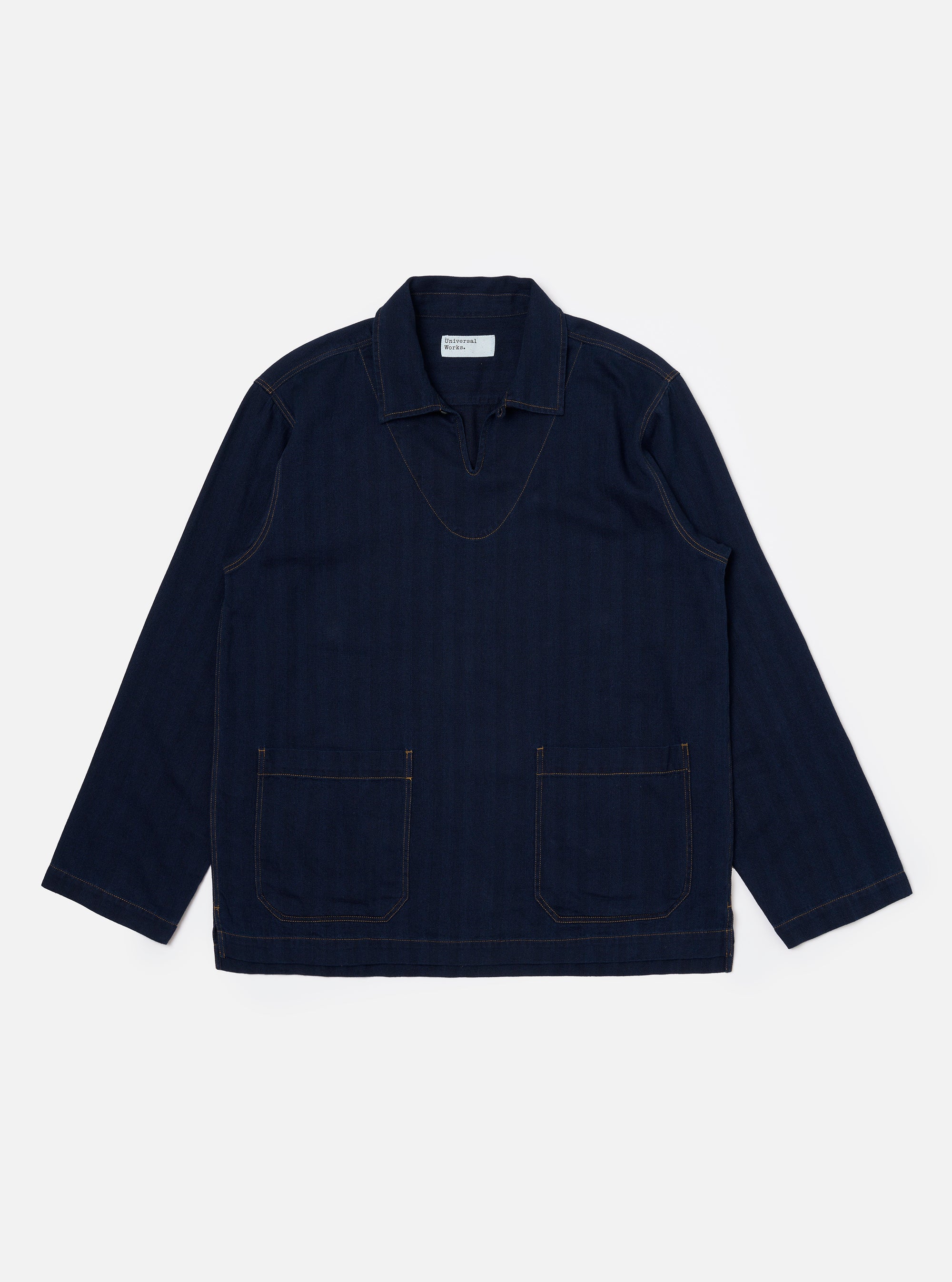 The Indigo Recycled Herringbone Smock Overshirt is shown as a flat lay against a plain white background. The overshirt features a partial button-down placket, a large chest patch pocket on the left side, and a simple collar. The dark indigo fabric has a visible herringbone weave texture.