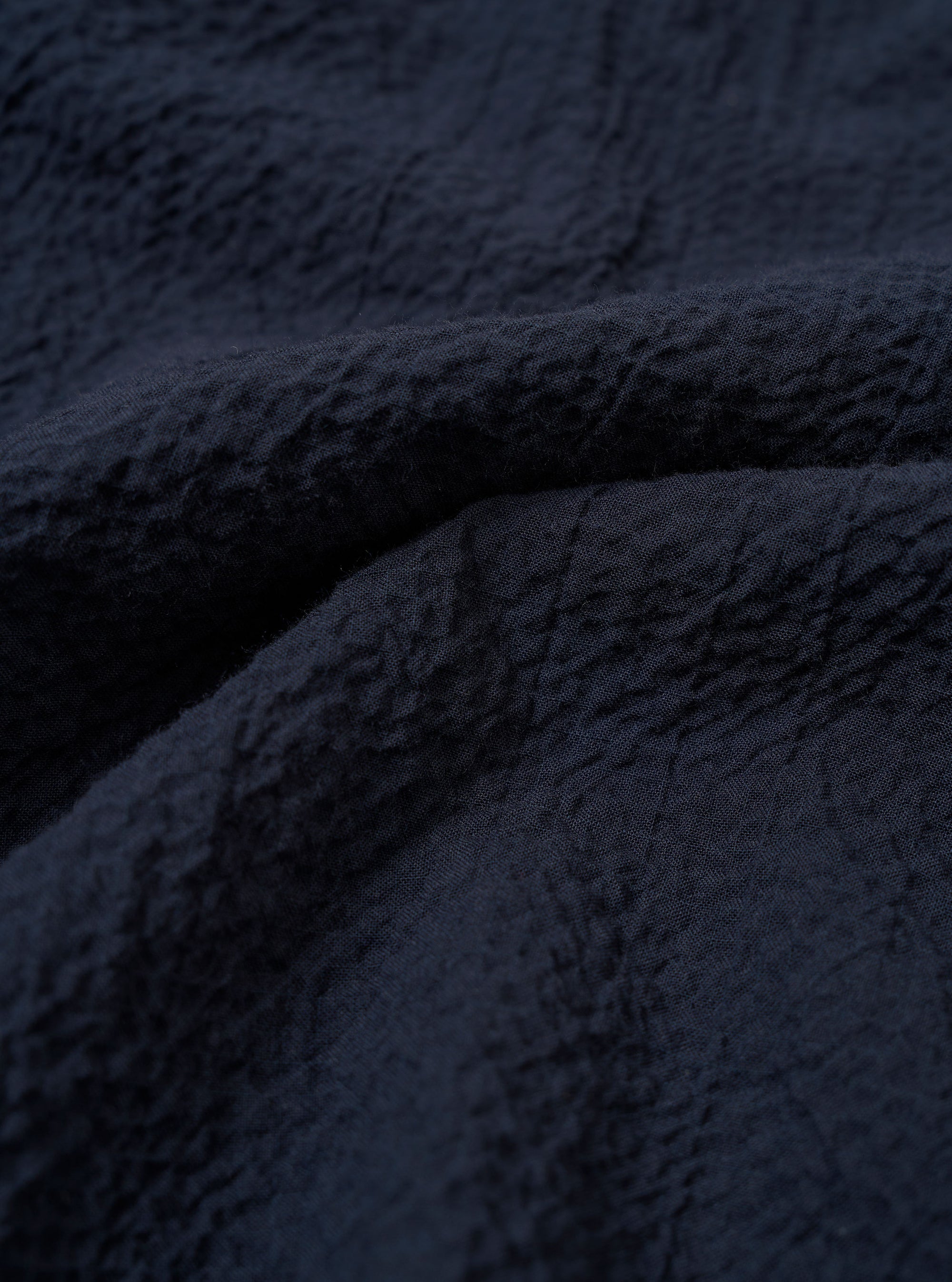 A close-up fabric swatch of the Navy Seersucker Shirting Lucky Shirt highlights the deep navy blue color and the distinct puckered texture of the seersucker material. The image provides a detailed view of the cotton fabric's weave and consistent tone.
