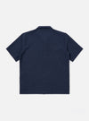 The Navy Seersucker Shirting Road Shirt is shown from a rear angle as a flat lay against a plain white background. The image highlights the shirt's short sleeves, straight hem, and the subtle puckered texture of the navy blue seersucker fabric. A small locker loop is visible at the center of the back yoke.