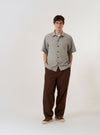 The Grey Izumi Cotton S/S Fatigue Shirt is shown as a flat lay against a plain white background. The shirt features a classic collar, a central button-down front, and two prominent patch pockets on the chest. The garment has short sleeves and is made from a textured grey cotton fabric.