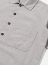 The Grey Izumi Cotton S/S Fatigue Shirt is shown in a detail view as a flat lay against a plain white background. The image highlights the textured, slubby character of the grey cotton-linen fabric and the contrasting white stitch detailing along the collar and seams.