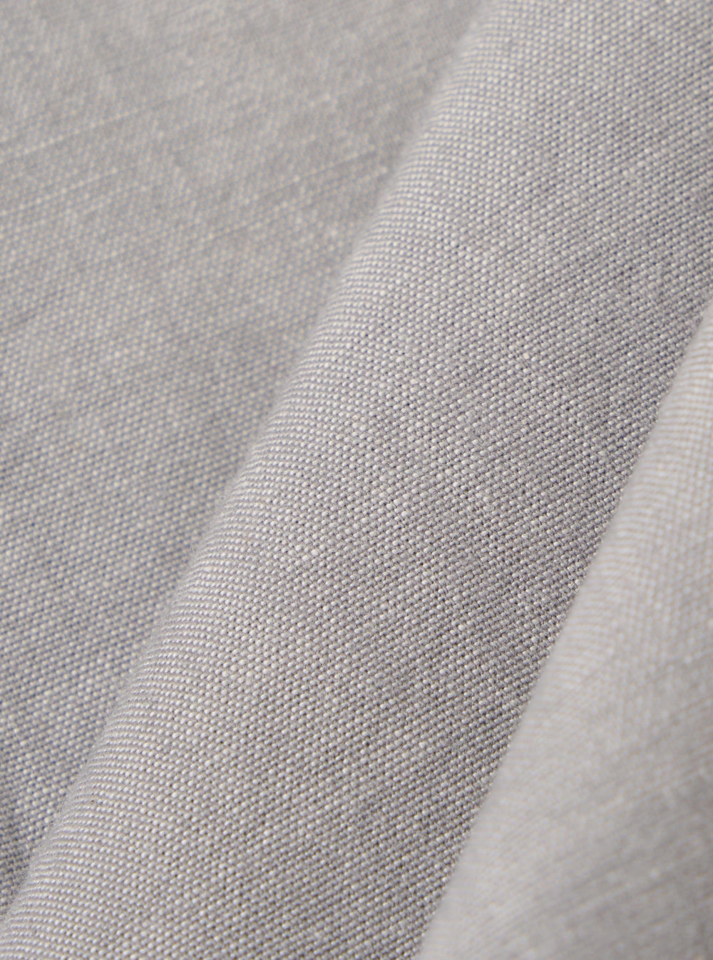 A close-up fabric swatch of the Grey Izumi Cotton S/S Fatigue Shirt highlights the grey color and the specific texture of the cotton material. The fabric fills the frame, providing a detailed view of the weave.