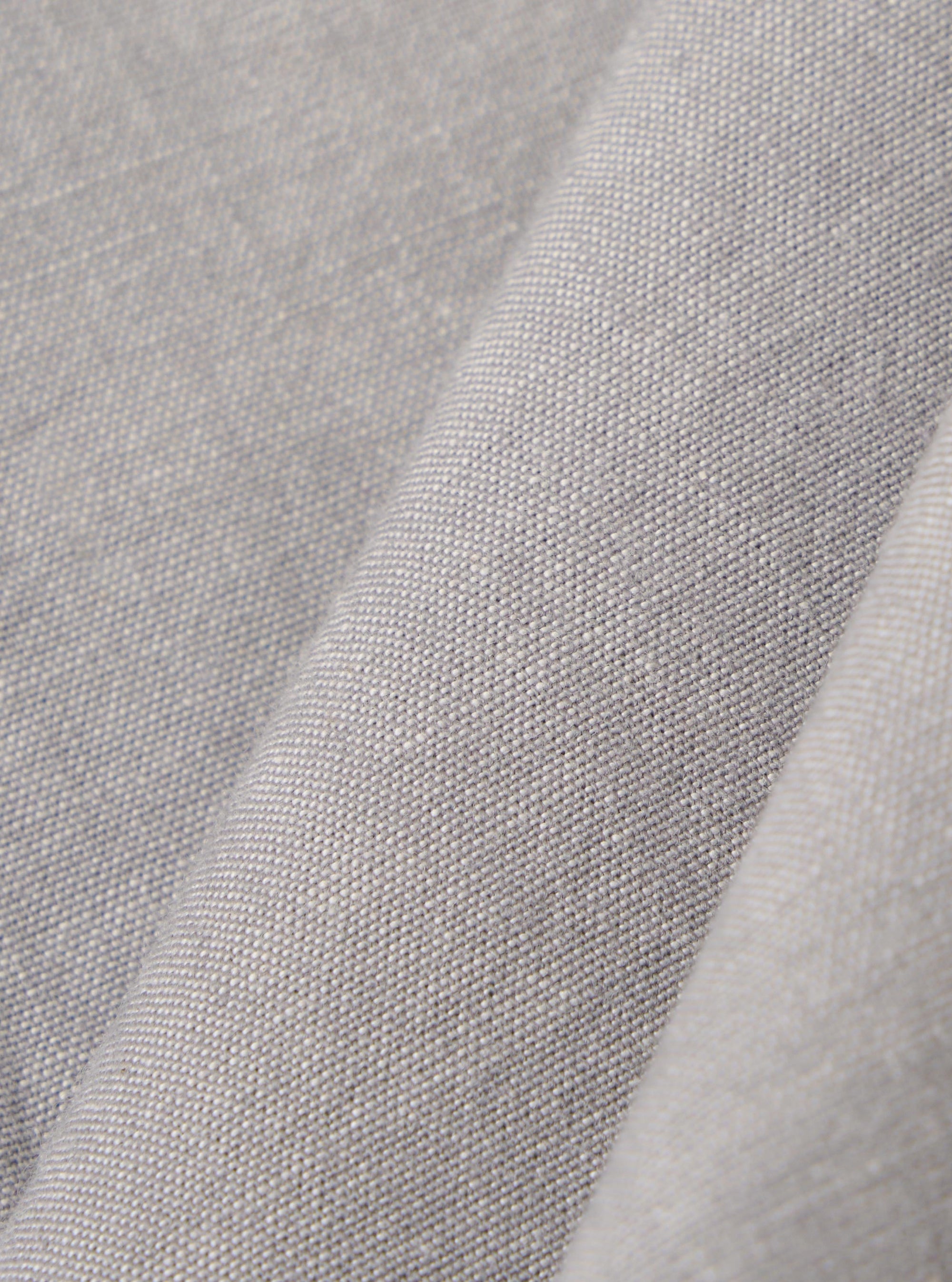 A close-up fabric swatch of the Grey Izumi Cotton S/S Fatigue Shirt highlights the grey color and the specific texture of the cotton material. The fabric fills the frame, providing a detailed view of the weave.