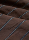 A close-up fabric swatch of the Brown Chester Stripe Oxford Pant highlights the texture and pattern of the material. The image displays a brown base with thin, light-colored vertical stripes across the cotton fabric.
