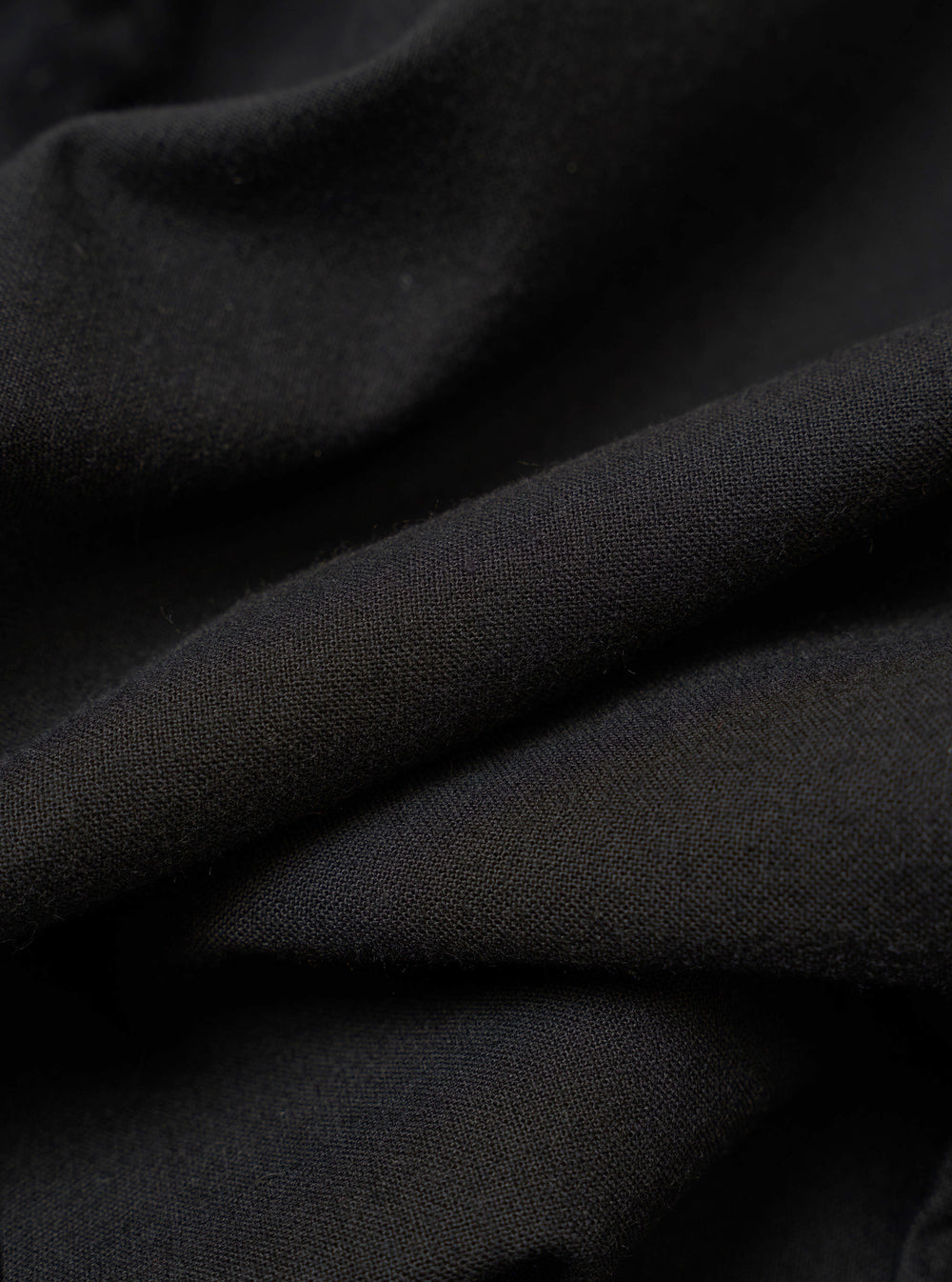 The Black Valencia Cotton Two Button Jacket is shown in a detail view as a flat lay against a plain white background. The image highlights the textured weave of the black cotton-blend fabric and the construction of the lower front patch pocket.