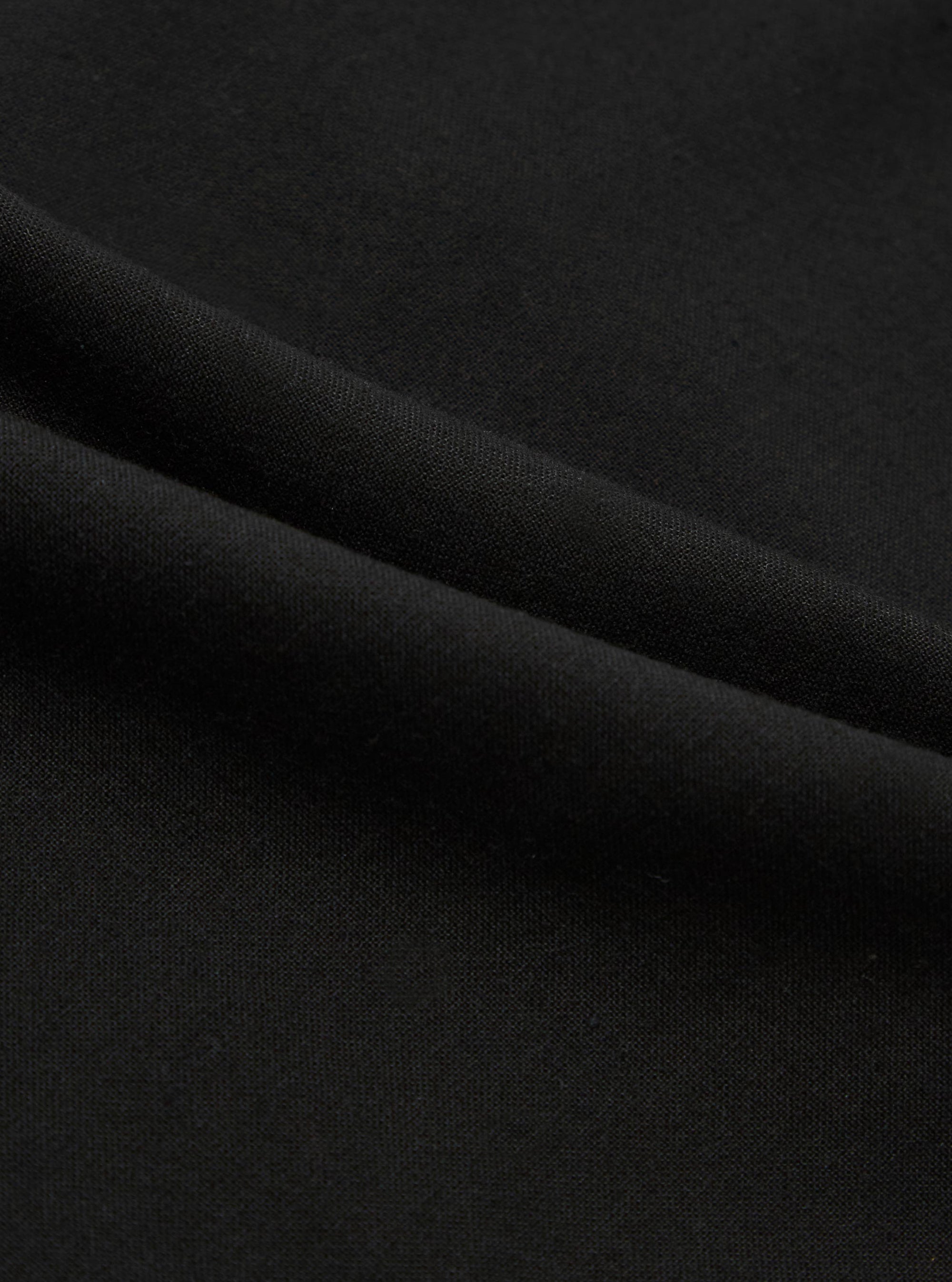 A close-up fabric swatch of the Black Valencia Cotton Military Chino displays the solid black color and the fine, woven texture of the Valencia cotton blend. The material fills the entire frame, providing a detailed view of the fabric's surface.