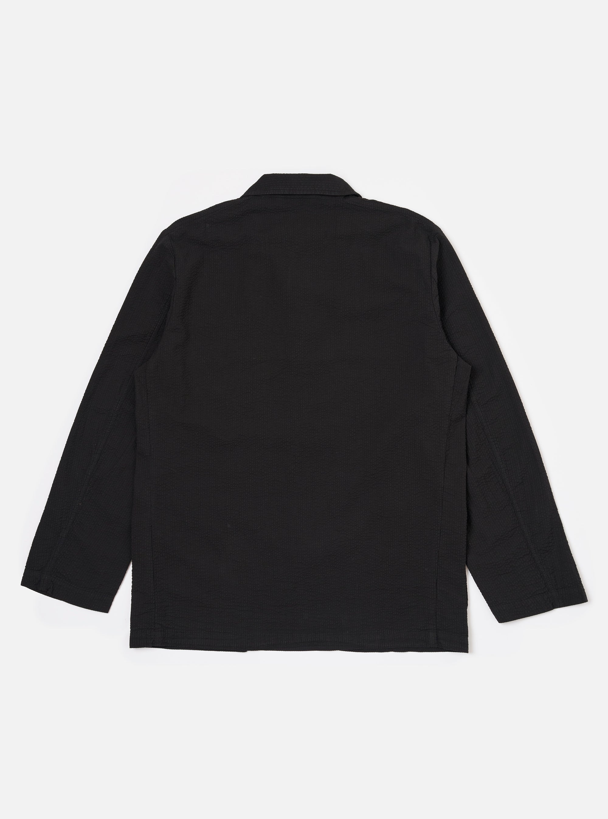 The Black Merida Seersucker Three Button Jacket is shown from the back as a flat lay against a plain white background. The image highlights the jacket's structured back panel, central vent at the hem, and the subtle puckered texture of the black seersucker fabric.