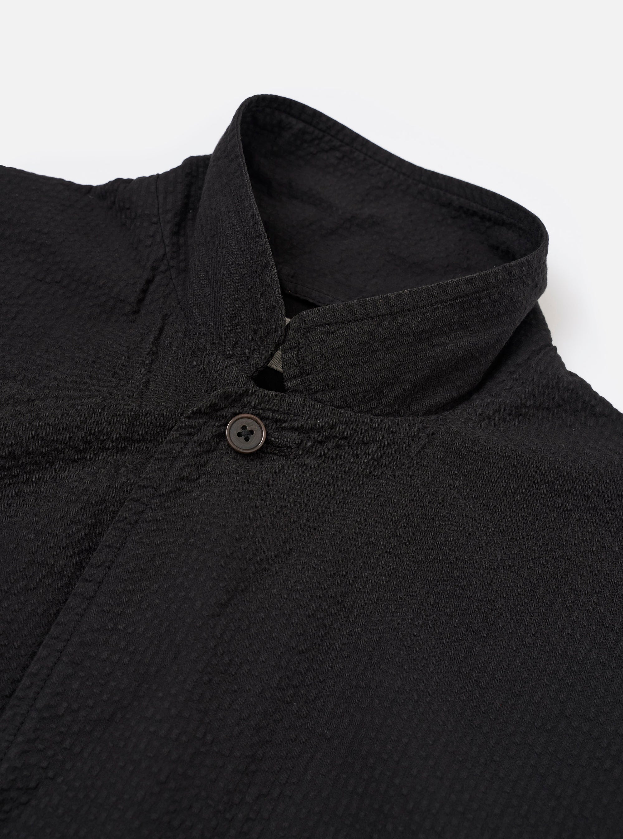 The Black Merida Seersucker Three Button Jacket is shown from the back as a flat lay against a plain white background. The image highlights the jacket's unstructured design, a central vertical seam, and the puckered texture of the black seersucker fabric.