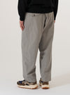 A model wears the Grey Izumi Cotton Oxford Pant against a plain white background. Shown from the waist down, the trousers feature a loose, wide-leg fit and a pleated front. The grey Izumi cotton fabric is detailed with a drawstring at the waist and functional side pockets.