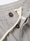 The Grey Izumi Cotton Oxford Pant is shown from the back as a flat lay against a plain white background. The image highlights the elasticated waistband and the two distinct rear pockets: one with a buttoned flap and one button jetted pocket. The trousers are a solid grey color and feature a wide leg cut.