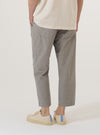 A model wears the Grey Izumi Cotton Hi Water Trouser, shown from the waist down from a rear angle against a plain white background. The trousers feature a slim, cropped fit, an elasticated waistband with a drawstring, and two large rear patch pockets. The grey cotton fabric has a visible textured appearance.