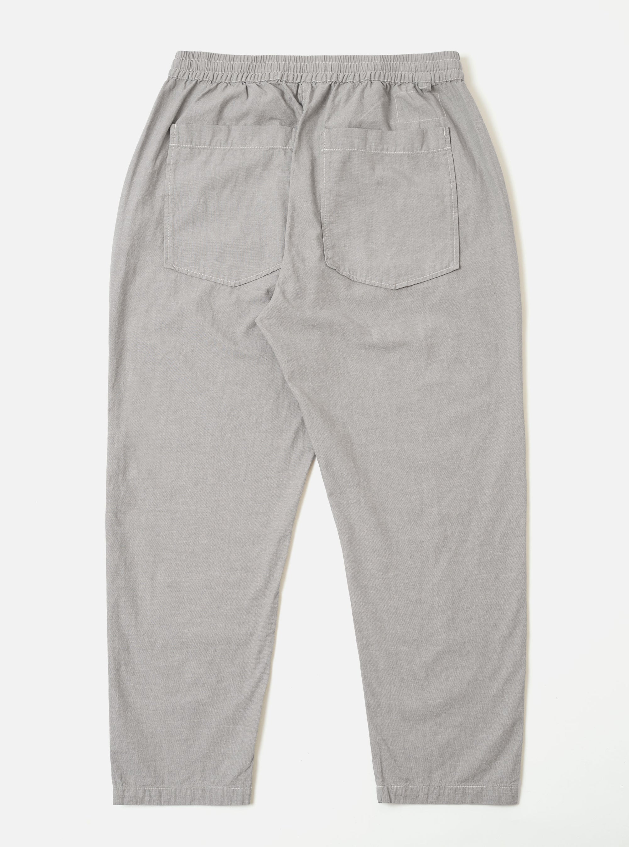 The Grey Izumi Cotton Hi Water Trouser is shown from the back as a flat lay against a plain white background. The image highlights the two rear button-down flap pockets and the elasticated waistband with a visible drawstring. The grey cotton fabric features a subtle, textured weave.