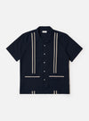 The Navy Classic Oxford Tropicana Shirt is shown as a flat lay against a plain white background. The shirt features a one-piece collar, a five-button front closure, and short, loose sleeves. Two large patch pockets are prominent on the lower front, and tonal inset embroidery detail is visible. The hem includes side splits and is longer at the back.
