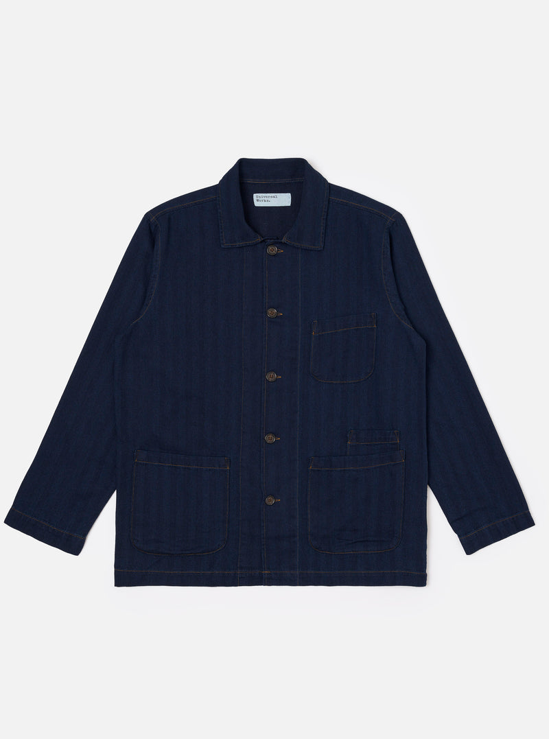 The Indigo Recycled Herringbone Bakers Overshirt is shown as a flat lay against a plain white background. The overshirt features a one-piece collar, a central button-down front, and four front patch pockets: one asymmetric pocket at the chest and three lower pockets including a small coin pocket. The indigo-dyed fabric displays a visible herringbone weave texture throughout.