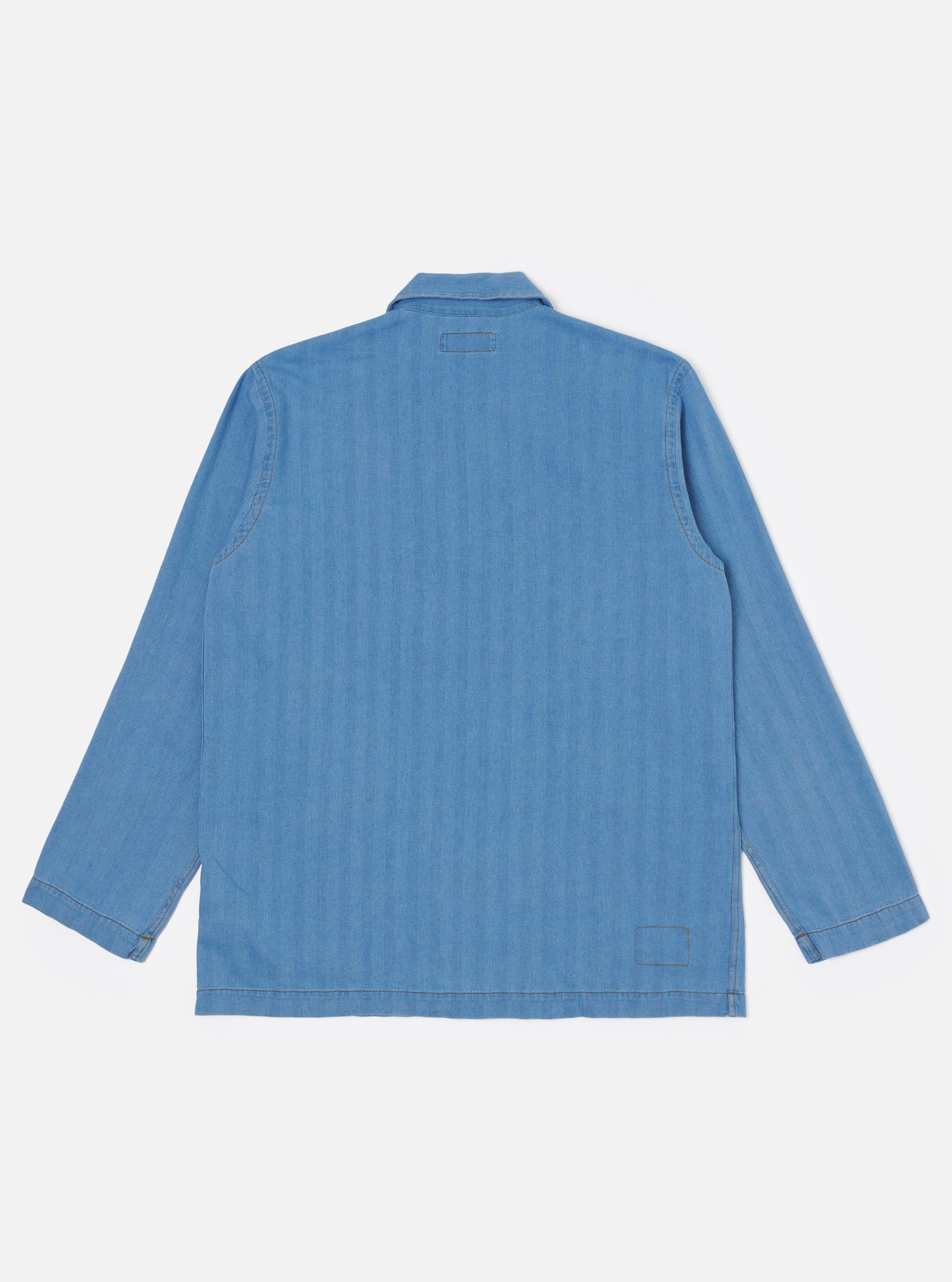 The Washed Indigo Recycled Herringbone Bakers Overshirt is shown from the back as a flat lay against a plain white background. The image highlights the textured herringbone weave of the washed indigo fabric, a straight hem, and a simple one-piece back panel with a central vertical seam.