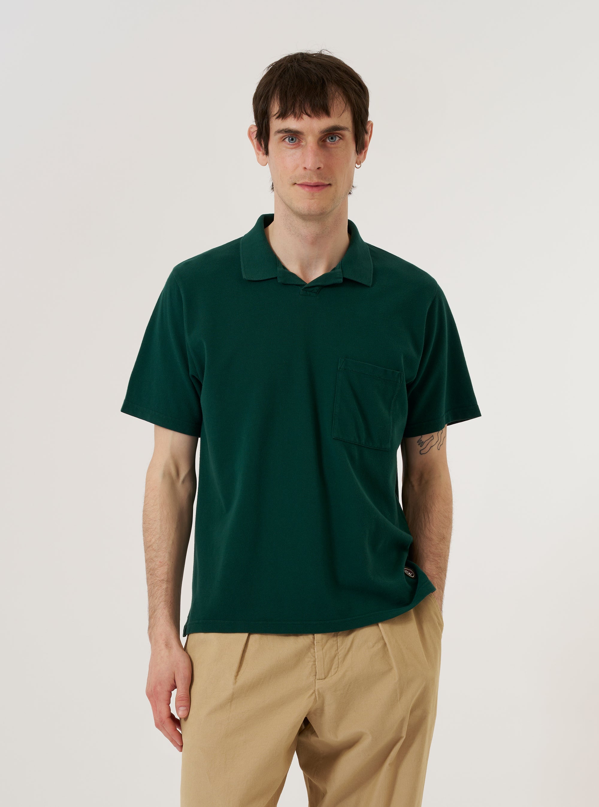 A model wears the Green Piquet Vacation Polo against a plain white background. The polo features a classic collar, a three-button placket, and a short-sleeved design with a textured piquet finish. The model is shown from the waist up, facing forward with the shirt neatly buttoned.