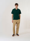 The Green Piquet Vacation Polo is shown as a flat lay against a white background. The polo features a relaxed single-piece collar, a three-button placket, and a single patch pocket on the left chest. The cotton piquet fabric has a distinctively fine textured weave, and the garment is finished with a straight hem and small side vents.