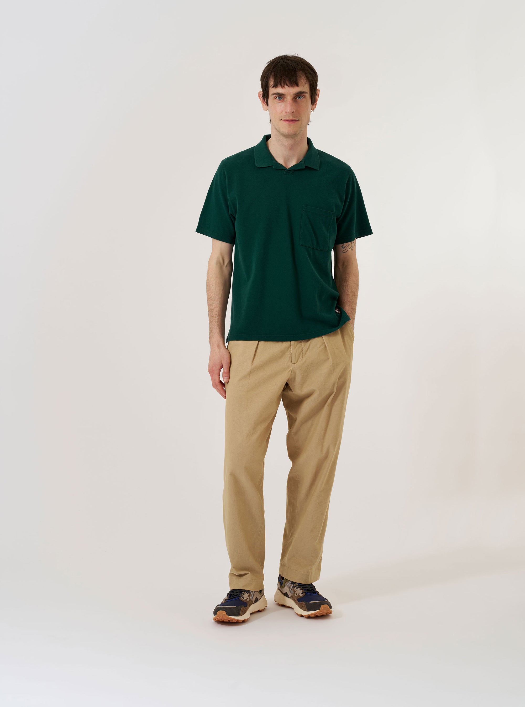 The Green Piquet Vacation Polo is shown as a flat lay against a white background. The polo features a relaxed single-piece collar, a three-button placket, and a single patch pocket on the left chest. The cotton piquet fabric has a distinctively fine textured weave, and the garment is finished with a straight hem and small side vents.