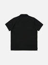 The Black Piquet Vacation Polo is shown from the back as a flat lay against a plain white background. The image highlights the clean, simple construction of the garment's rear panel, the short sleeves, and the classic polo collar. The black cotton piquet fabric has a visible fine-puckered texture.