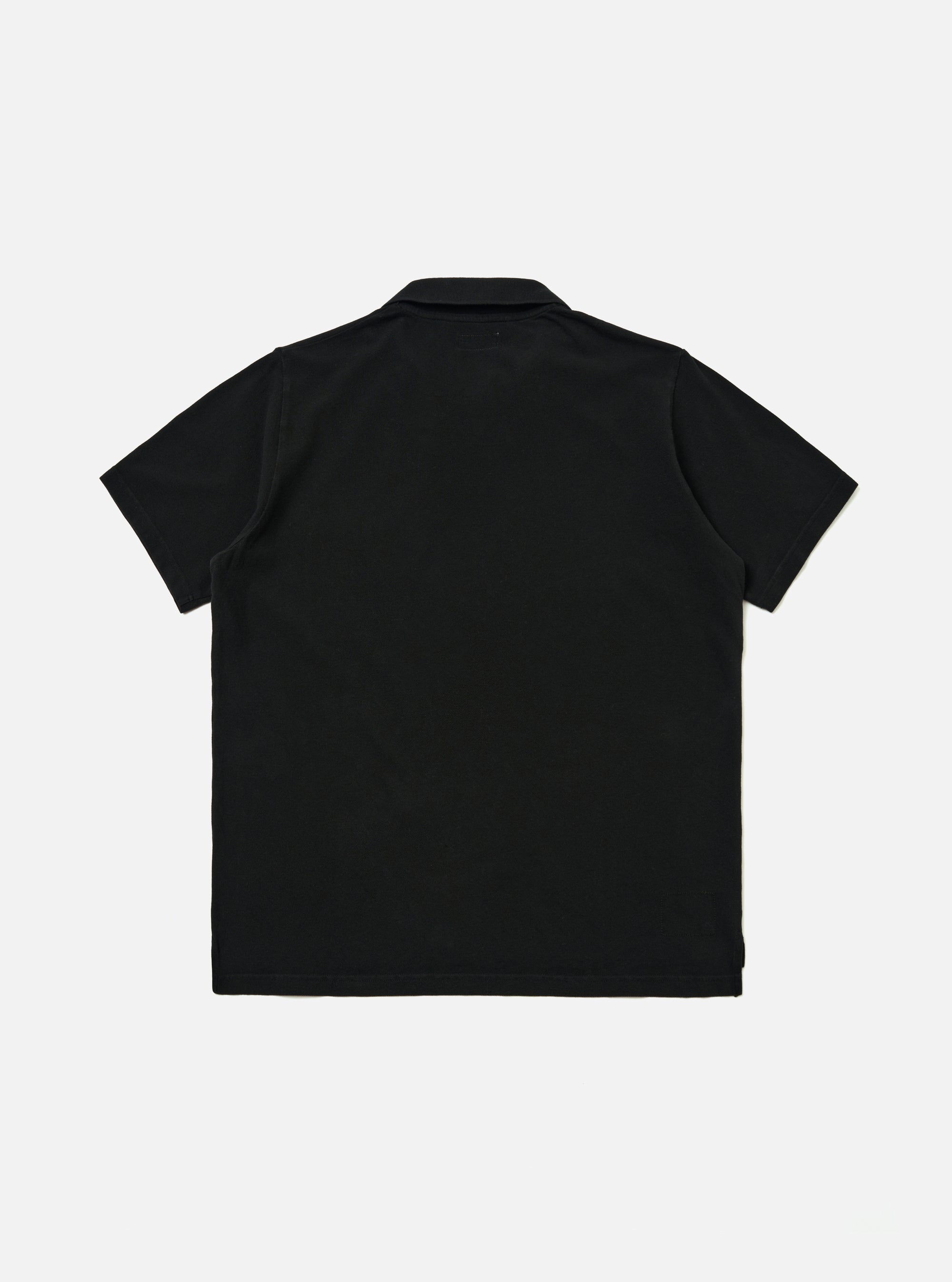 The Black Piquet Vacation Polo is shown from the back as a flat lay against a plain white background. The image highlights the clean, simple construction of the garment's rear panel, the short sleeves, and the classic polo collar. The black cotton piquet fabric has a visible fine-puckered texture.