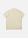 The Ecru Piquet Vacation Polo is shown from the back as a flat lay against a plain white background. The image highlights the clean construction of the garment's rear, the simple one-piece collar, and a dropped back hem with small side vents. The ecru-colored cotton fabric features a visible honey-comb piquet texture.