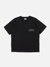 The Black Organic Jersey Print Pocket Tee is displayed as a flat lay against a plain white background. The T-shirt features a classic crew neckline, short sleeves, and a single patch pocket on the left chest area featuring a graphic print. The garment is made from a solid black organic cotton jersey fabric.