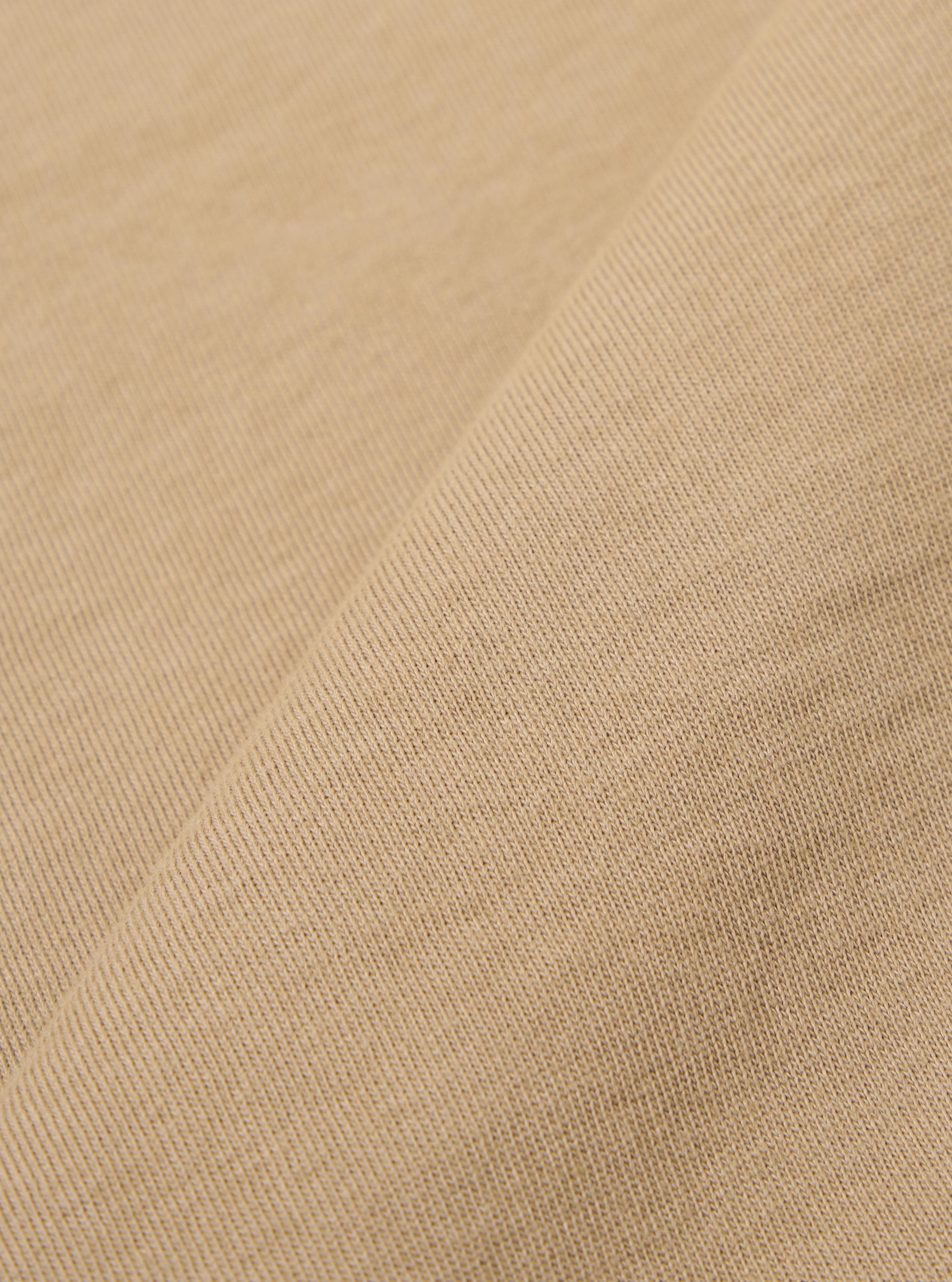 A close-up fabric swatch of the Sand Rugby Jersey Oversized Vacation Polo highlights the sand-colored organic cotton jersey material and its soft, knit texture. The fabric fills the frame, providing a detailed view of the garment's color.