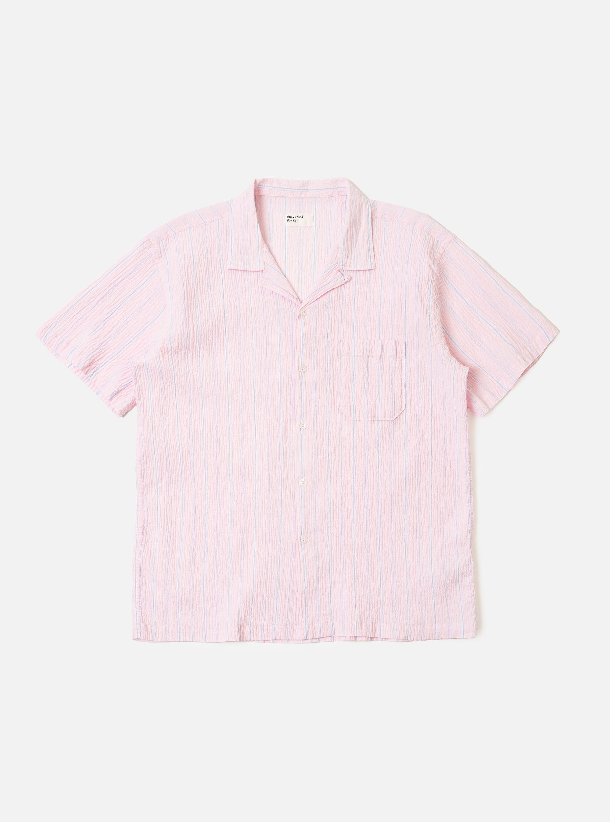 The Pink Lily Stripe Road Shirt is shown as a flat lay against a white background. The short-sleeve shirt features a pink and white vertical pinstripe pattern, a single chest patch pocket on the left side, and a straight hem. The camp collar is open-necked with a visible loop closure at the top. The fabric has a fine seersucker texture.