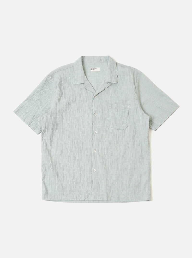The Green Seersucker Road Shirt is shown as a flat lay against a white background. The shirt features a camp collar, a button-front closure with tonal buttons, and a straight hem. The fabric has a distinctive puckered seersucker texture in a solid green color.