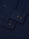 The Indigo Recycled Herringbone Attendant Shirt is shown from the back as a flat lay against a white background. The shirt features a straight hem, a single horizontal yoke across the shoulders, and a simple flat collar. The indigo fabric has a visible vertical herringbone texture throughout.