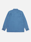 The Washed Indigo Recycled Herringbone Attendant Shirt is shown from the back as a flat lay against a plain white background. The image highlights the textured herringbone weave of the washed indigo fabric and the clean, simple construction of the garment's rear panel, featuring a straight hem.