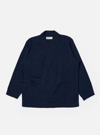 The Indigo Recycled Herringbone Kyoto Work Jacket is shown as a flat lay against a white background. The jacket features a collarless, wrap-style front with fabric ties, two large patch pockets at the waist, and one patch pocket on the left chest. The indigo-colored fabric has a visible herringbone weave texture.