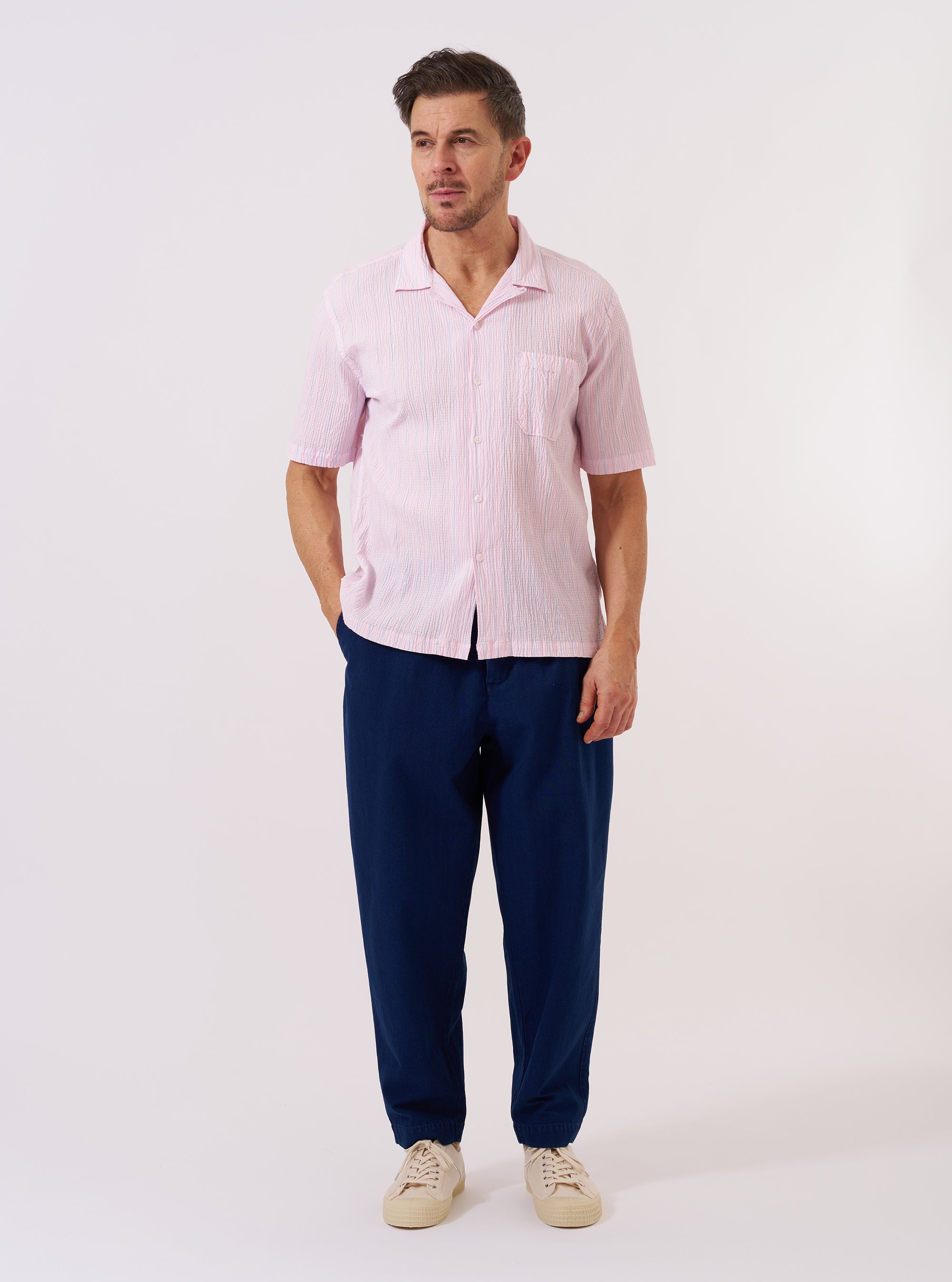 The Pink Lily Stripe Road Shirt is displayed as a flat lay against a white background. The shirt features a camp collar, a single chest pocket, and a front button closure. The design consists of vertical stripes in shades of pink and red.