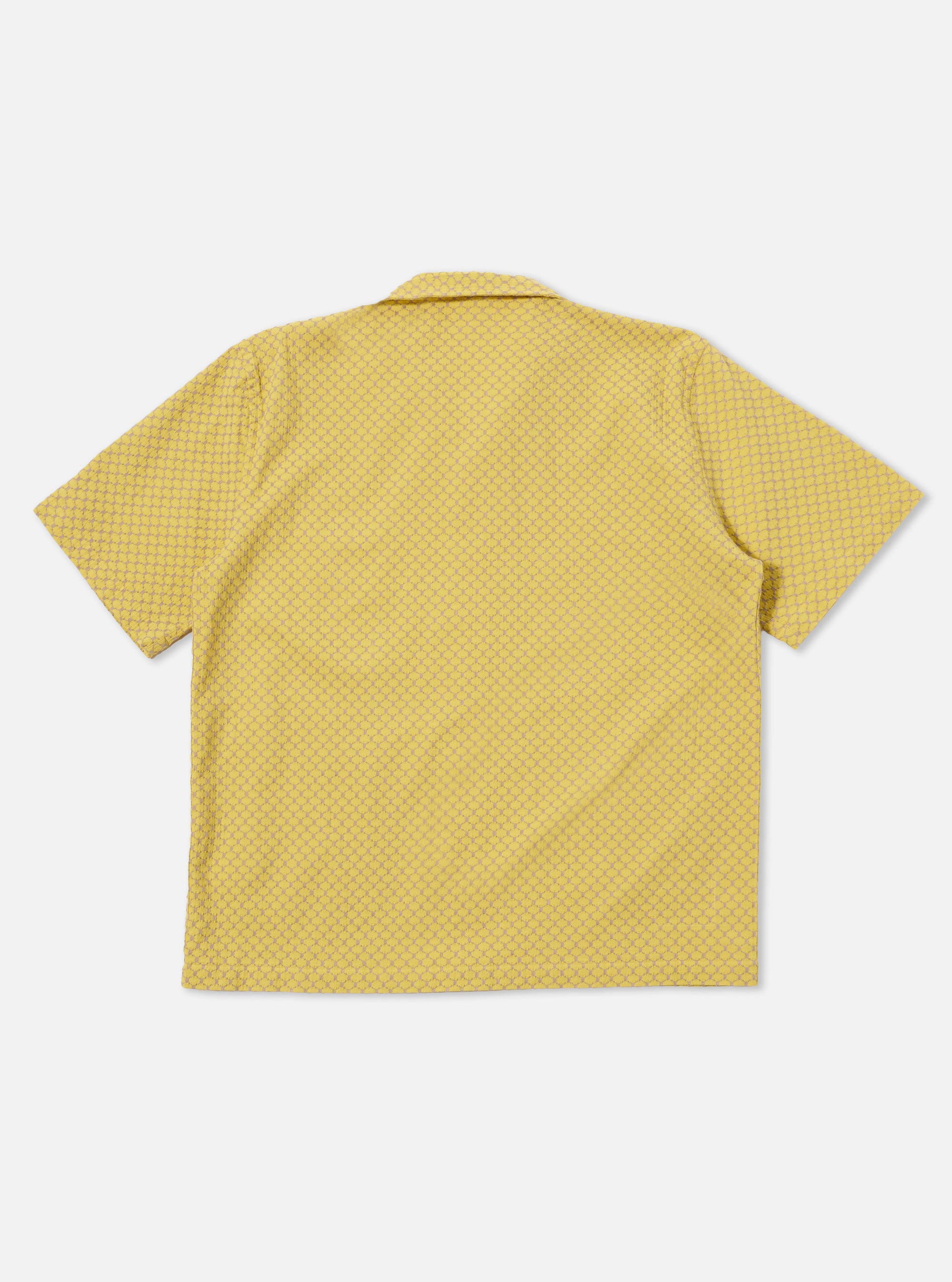 A model wears the Yellow Mykonos Cotton Road Shirt against a plain, neutral background. The short-sleeve shirt features a textured yellow and ochre pattern, a one-piece camp collar with a loop closure, and a single patch pocket on the left chest. The garment is shown with a regular fit and a straight hem.