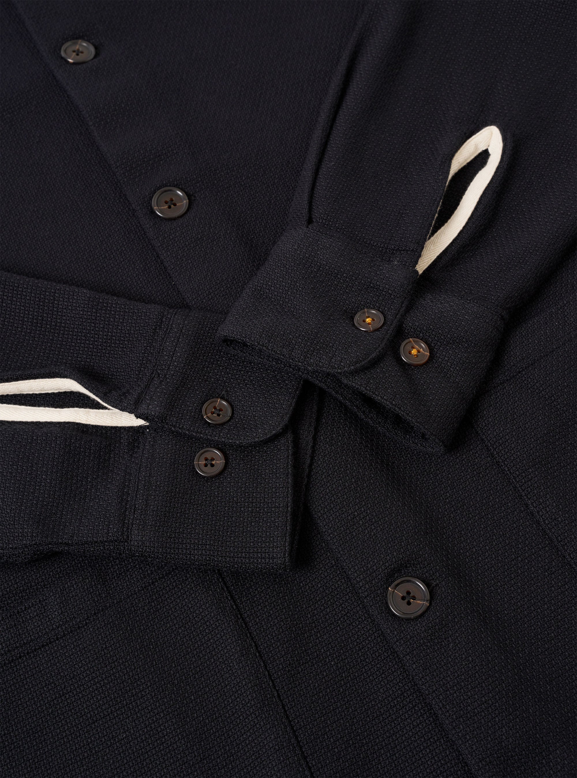 The Black Kendal Cotton Travail Overshirt is shown in a detail view as a flat lay against a plain white background. The image focuses on the texture of the black cotton fabric and the construction of a functional chest patch pocket.