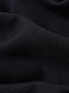 A close-up fabric swatch of the Black Kendal Cotton Travail Overshirt highlights the solid black color and the smooth, durable weave of the cotton fabric. The material fills the entire frame, providing a detailed view of the garment's texture.