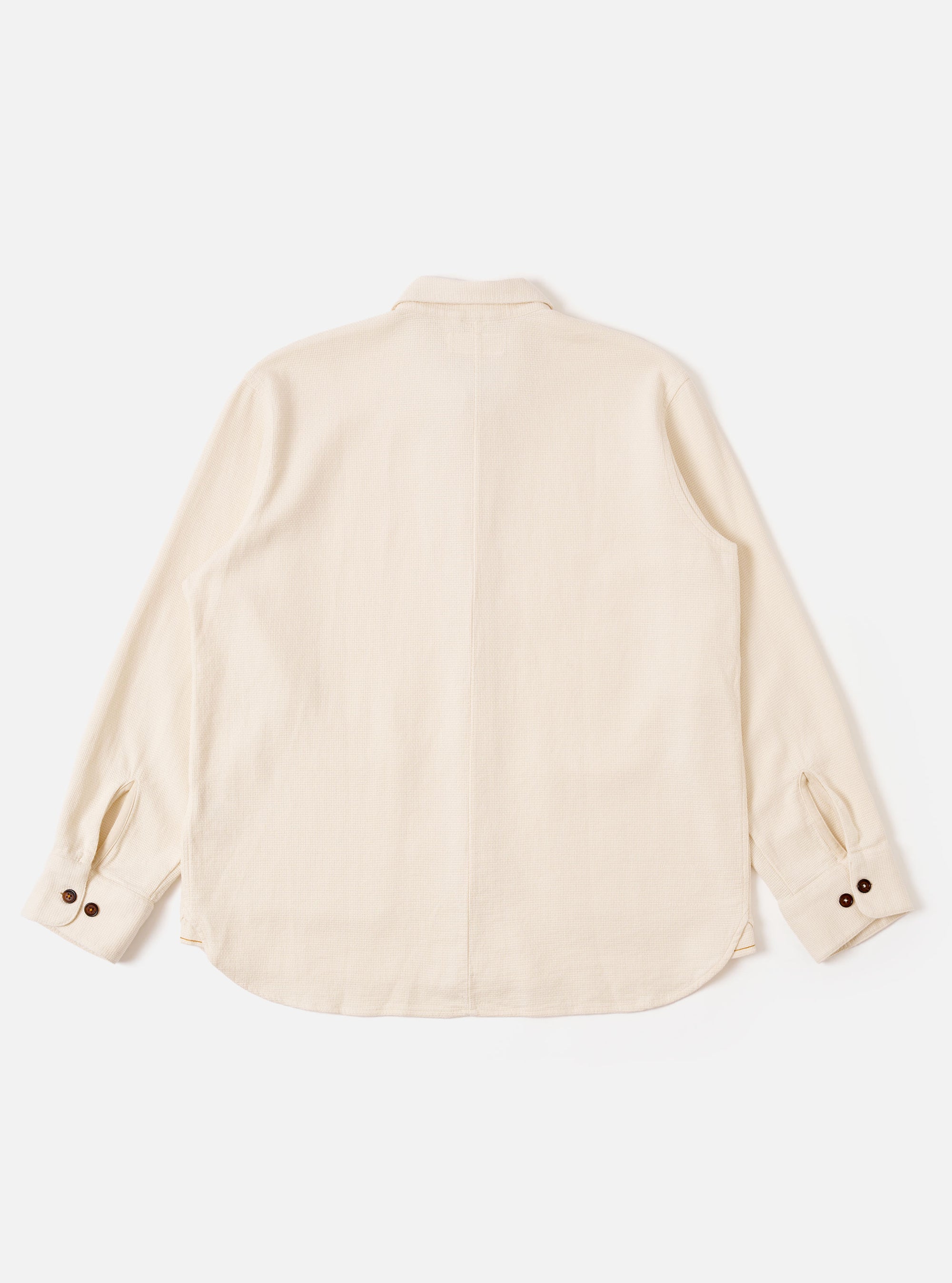 The Ecru Kendal Cotton Travail Overshirt is shown from the back as a flat lay against a plain white background. The image highlights the garment's curved hem, one-piece collar, and simple rear construction. The fabric is a solid ecru-colored cotton.